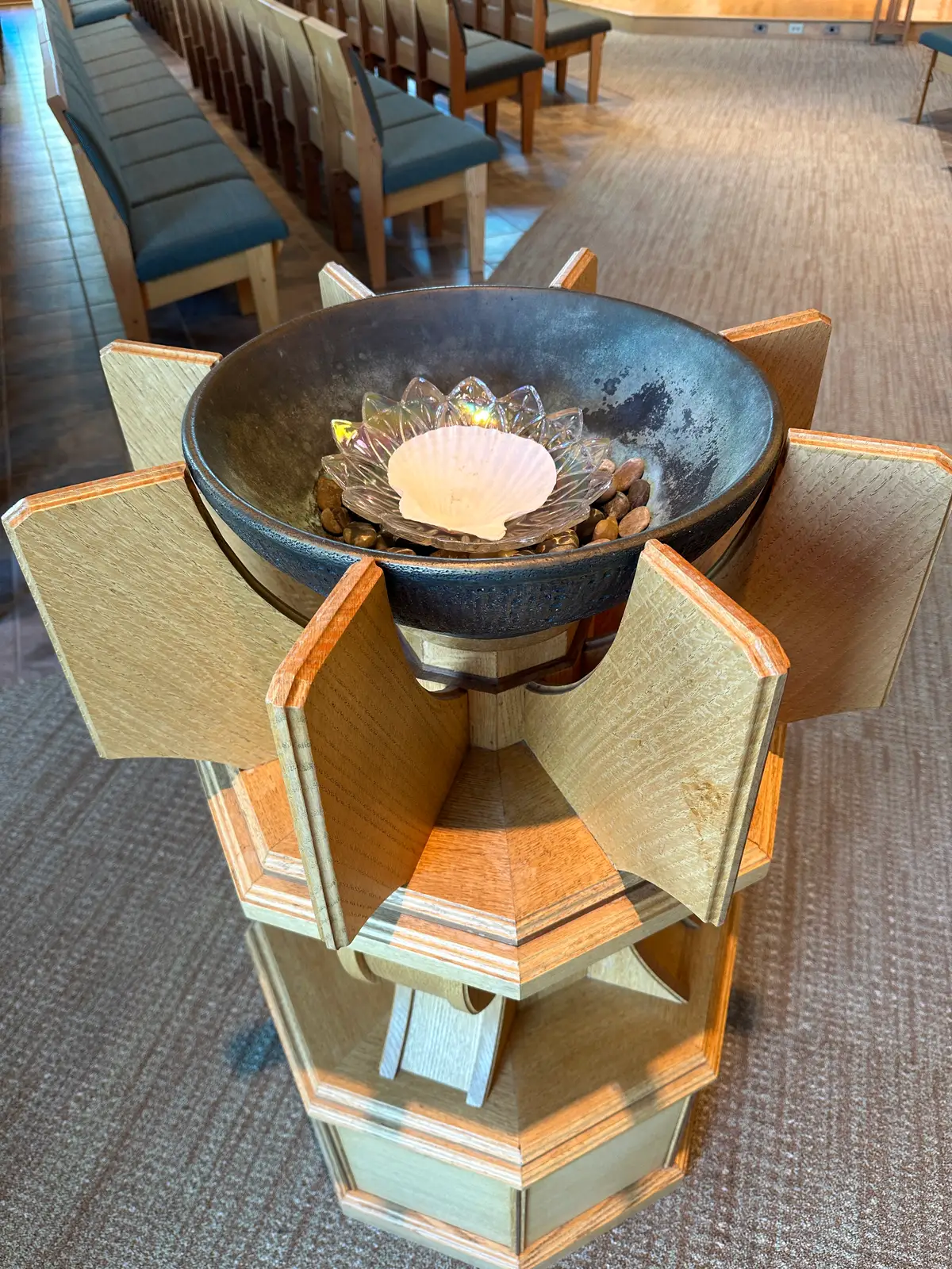 The baptismal font, a scallop shell in the bowl on a cross-shaped wooden pedestal.